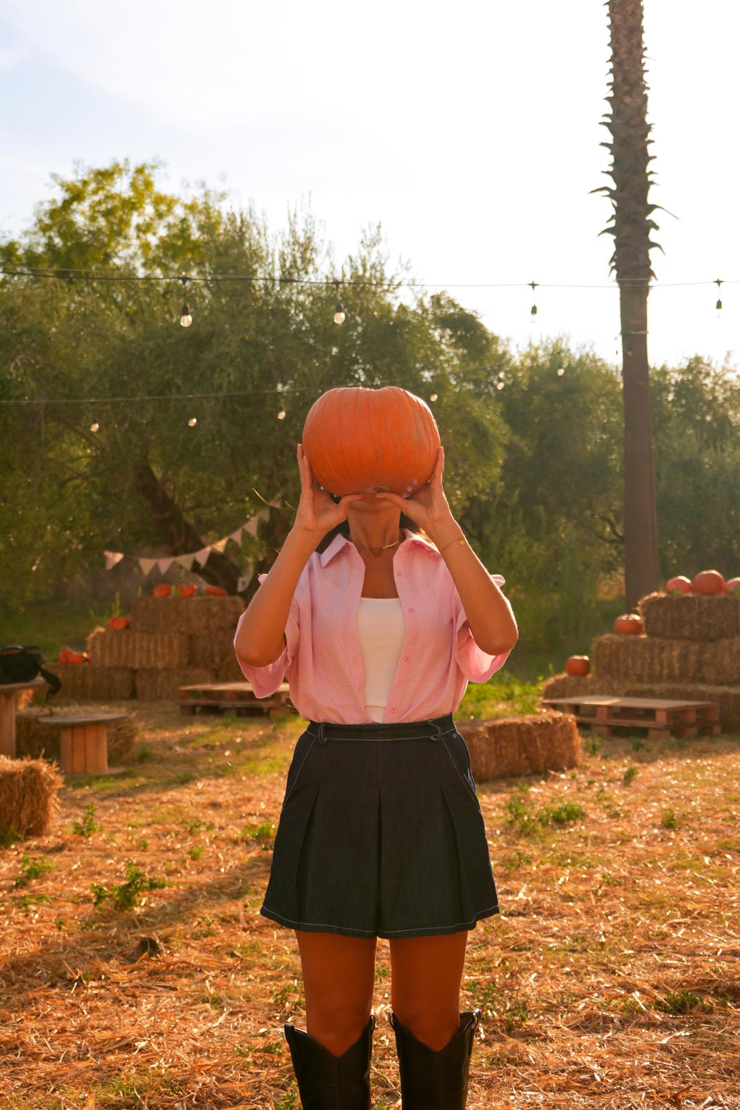 Una bambina tiene una zucca davanti al viso in mezzo al campo, fra gli ulivi e le bandierine